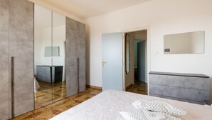 A bedroom with a large wardrobe, a bedside table, a bed with a floral bedspread, and a mirror on the wall. - 2 bedroom cozy home in Torre Chianca - Lecce (Torre Chianca - Lecce)