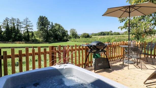 A hot tub with a wooden deck, a grill, and outdoor furniture.