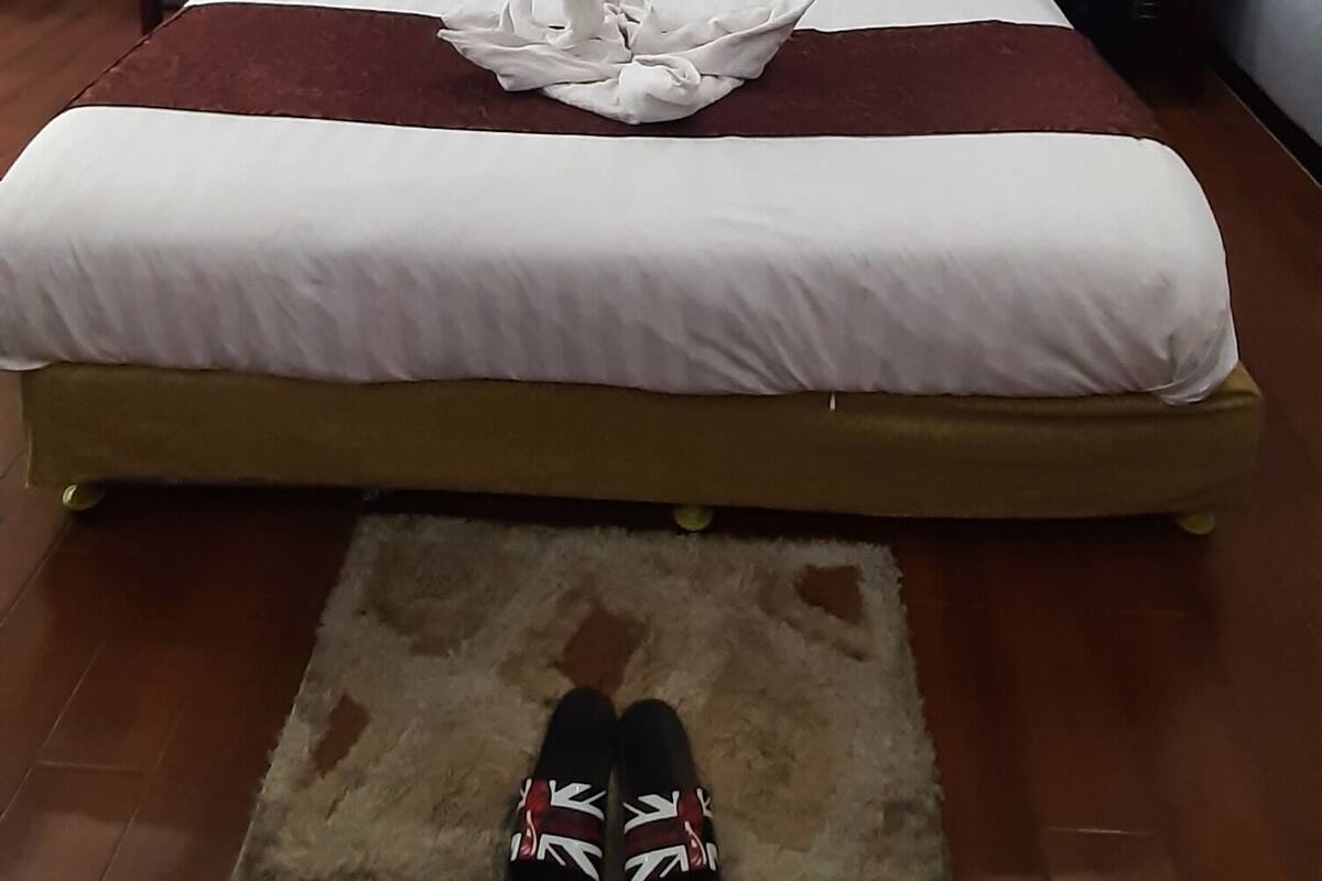 Ein ordentlich bezogenes Bett mit weißen Leinen, einem braunen Kopfteil und einem Paar Schuhe auf einem Teppich.