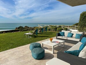 Eine Terrasse mit Gartenmöbeln, einem weißen Couchtisch und Blick auf den Ozean.