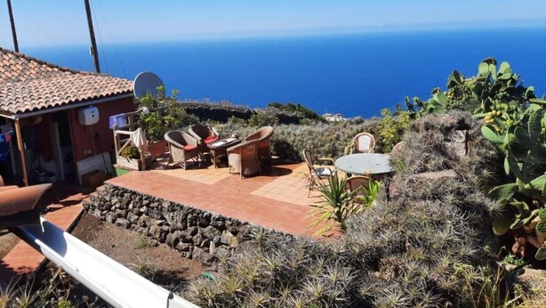 Un pati amb mobles d'exterior, un edifici petit amb antena parabòlica i vista a l'oceà.