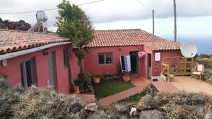 Una casa amb teulada vermella, antenes satèl·lit i un petit jardí amb cactus, i una cadira de fusta a l'exterior.