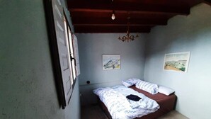 Un dormitori petit i acollidor amb un llit individual, un sostre de fusta i dos quadres penjats a la paret.