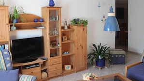 Ein Wohnzimmer mit Fernseher, Holzschränken, einer Couch, einem Couchtisch und einer Pendelleuchte.