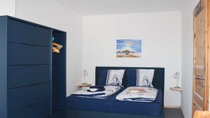 Ein Schlafzimmer mit einem Bett, einem Kleiderschrank, einem Nachttisch, einer Lampe und einem Bild an der Wand.
