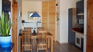 Eine kleine Küche mit Holzausstattung, einem Esstisch mit Stühlen, einem Blumentopf und einer Mikrowelle.