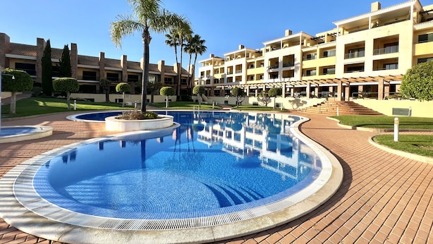 Um hotel com uma piscina grande, palmeiras e um caminho de tijolos.