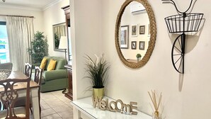 Uma sala de estar moderna com área de jantar, um espelho grande e um letreiro de boas-vindas.