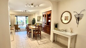 Uma ampla área de jantar com uma mesa grande e cadeiras, um lustre moderno no teto e uma placa acolhedora com a palavra 'Welcome'.