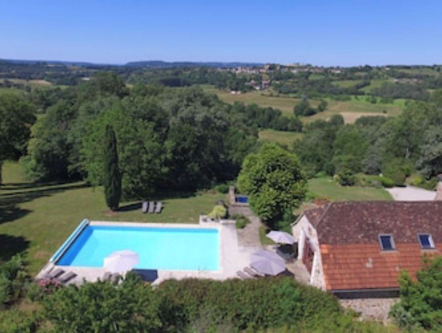 A residential property with a swimming pool, surrounded by lush greenery and a hilly landscape in the background.