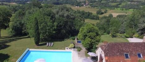 A residential property with a swimming pool, surrounded by lush greenery and a hilly landscape in the background.