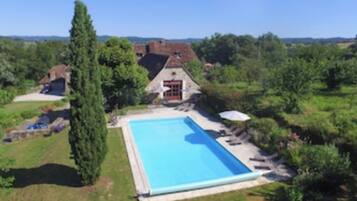 A large rectangular swimming pool surrounded by a lawn, with a stone building in the background.