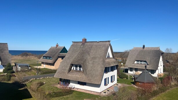 A row of thatched-roof cottages with white walls and dark shutters, set against a clear blue sky and a view of the sea. - 5 star hotel according to DTV - pure luxury, only 200m from the beach - WLAN free of charge (Dranske)