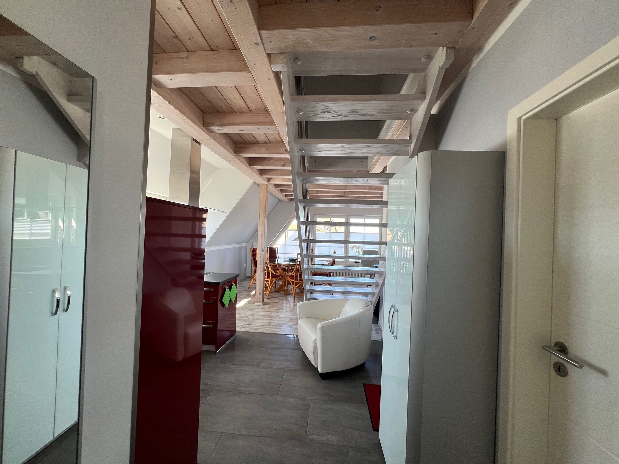 A modern interior with a staircase leading to a loft area, white and red cabinetry, and a seating area with a white sofa.