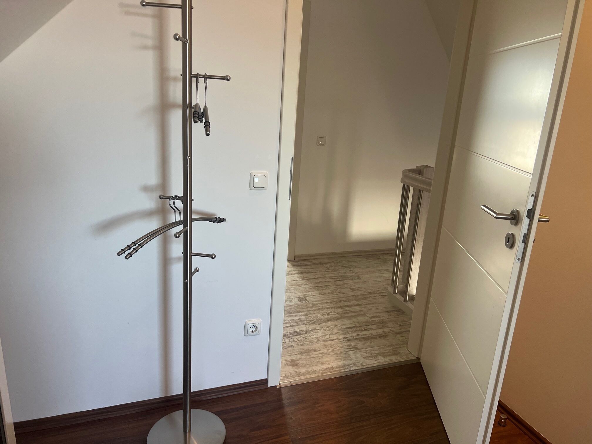 Un pasillo con un perchero, una puerta con pomo y un interruptor de luz en la pared.