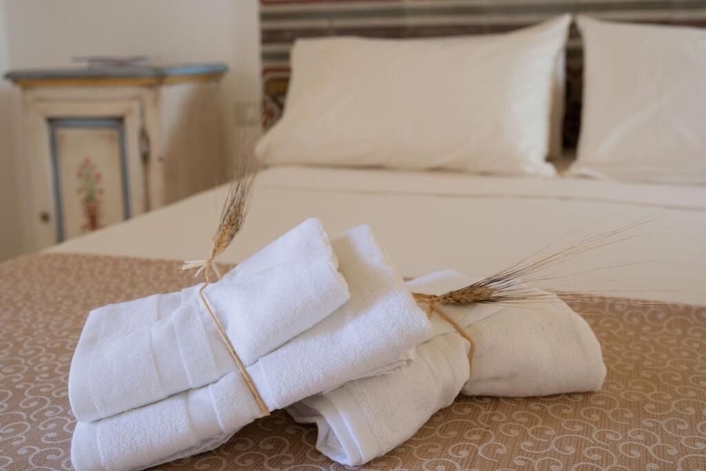 A neatly made bed with white linens and a decorative wheat stalk tied to the pillows.