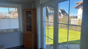 Une pièce avec un meuble en bois, une fenêtre avec des stores et une porte vitrée donnant sur une pelouse.