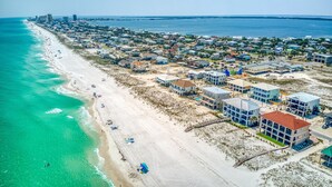 An aerial view of a coastal town with beachfront properties, a pier extending into the ocean, and a clear sky. - Beautiful 6 BR Gulf View Home | Private Pool | Pet Friendly | Event Friendly (Pensacola Beach)