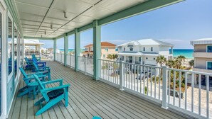 A covered balcony with blue chairs, a view of the beach, and houses in the background. - Beautiful 6 BR Gulf View Home | Private Pool | Pet Friendly | Event Friendly (Pensacola Beach)