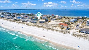An aerial view of a coastal residential area with beachfront properties, a pier, and a clear sky.