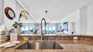 A modern kitchen with granite countertops, stainless steel sink, and a large window offering a view of the outdoors. - Adagio B-203 Beach Front 4/3 - Beautiful Unit with Beautiful Views! (Santa Rosa Beach)