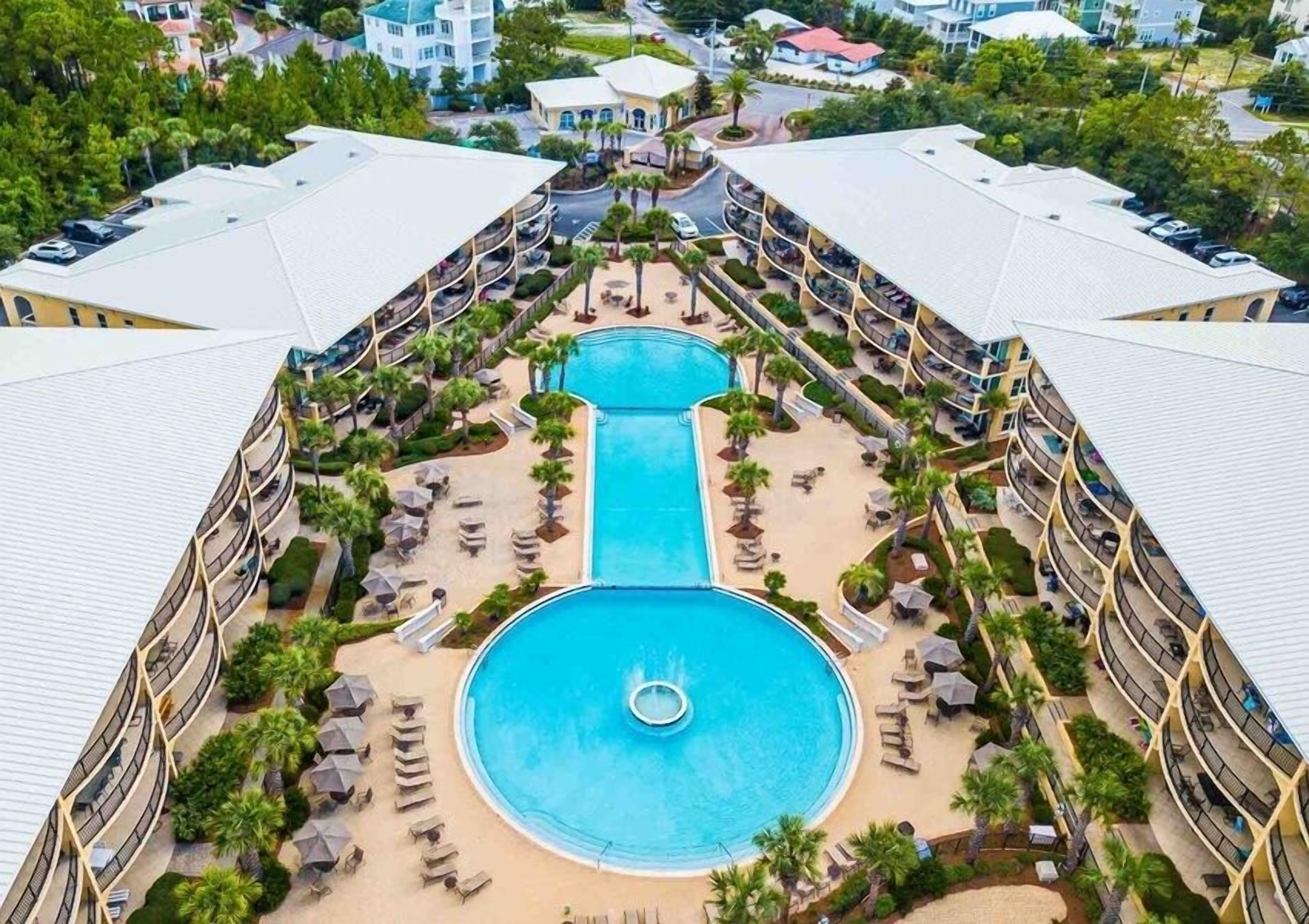 A resort with a central pool, multiple balconies, and surrounding palm trees.