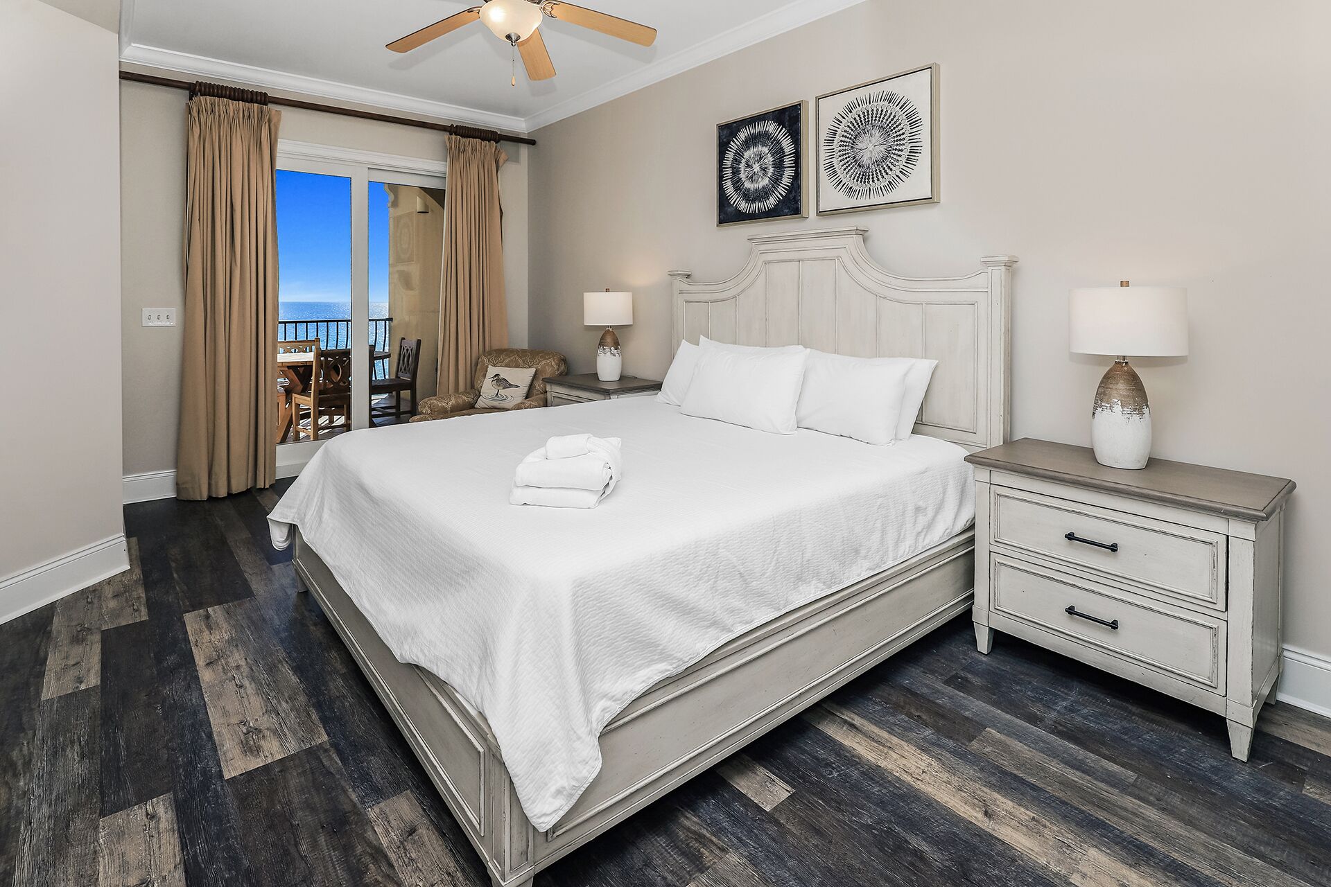 A hotel room with a large bed, a nightstand with a lamp, a chair, and a view of the ocean.