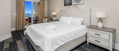A hotel room with a large bed, a nightstand with a lamp, a chair, and a view of the ocean.