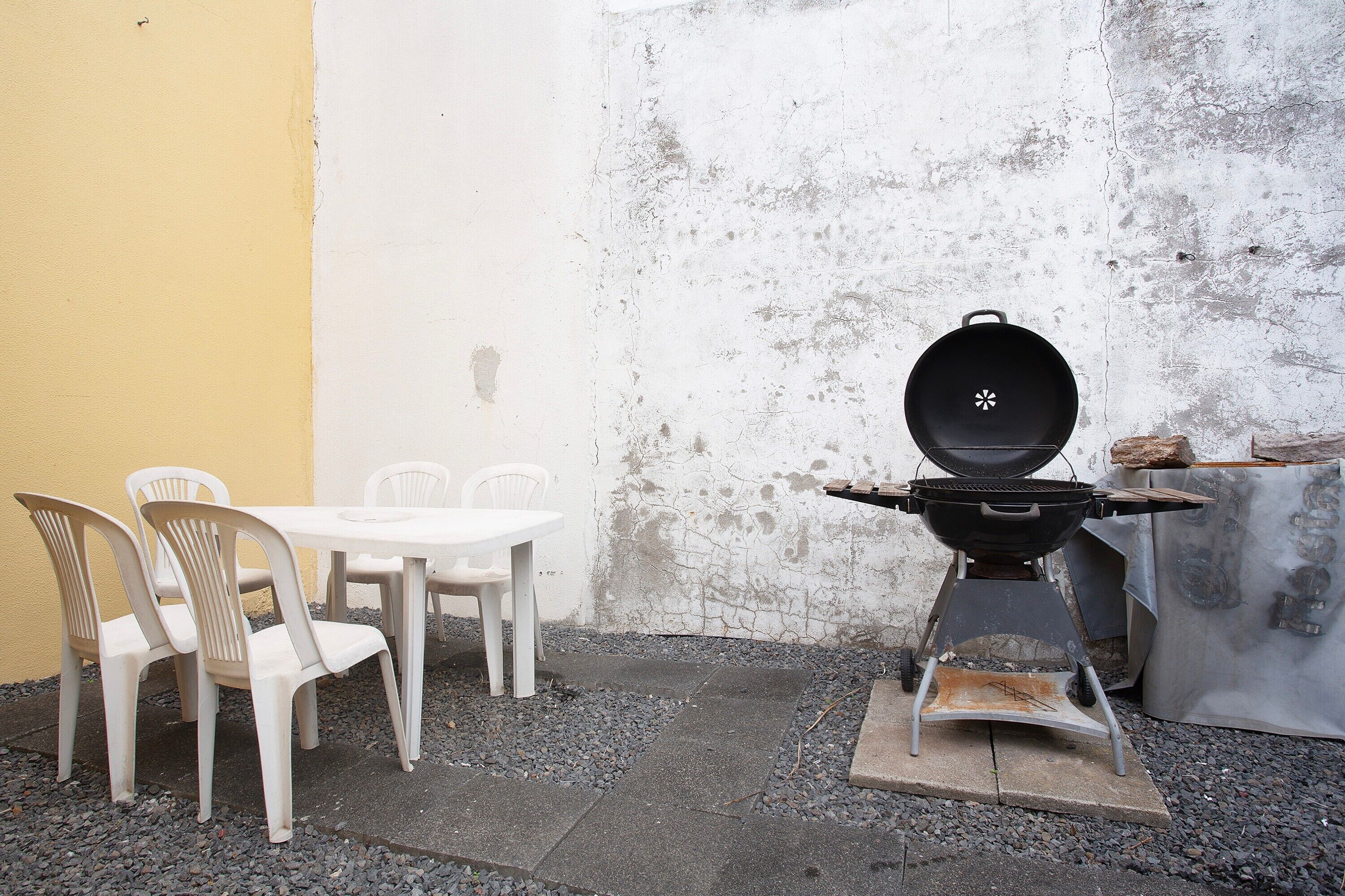 Une terrasse avec un barbecue, des chaises en plastique blanches et une table.
