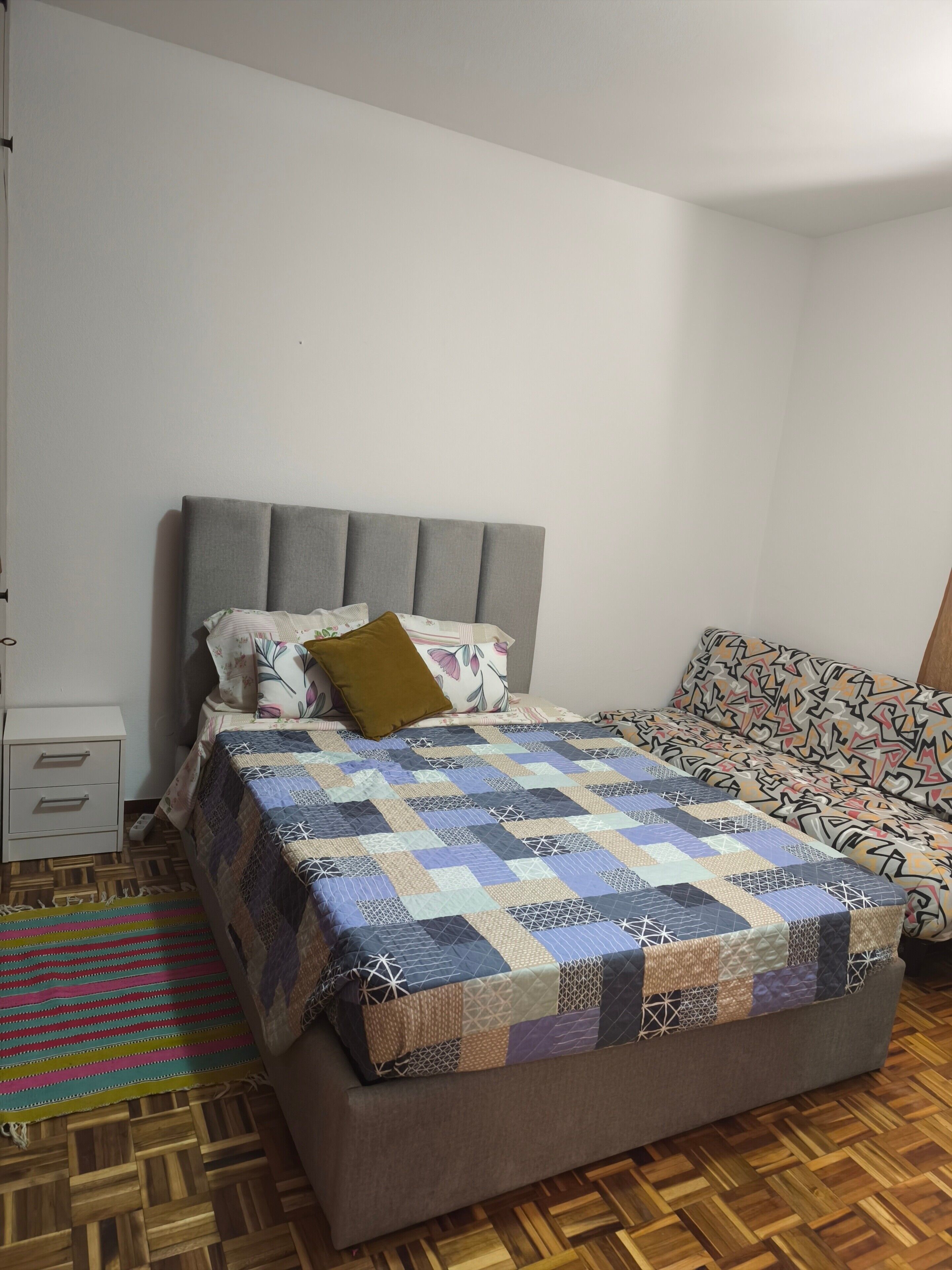Ein Schlafzimmer mit einem Bett, einem Nachttisch, einer gemusterten Couch und Holzboden.