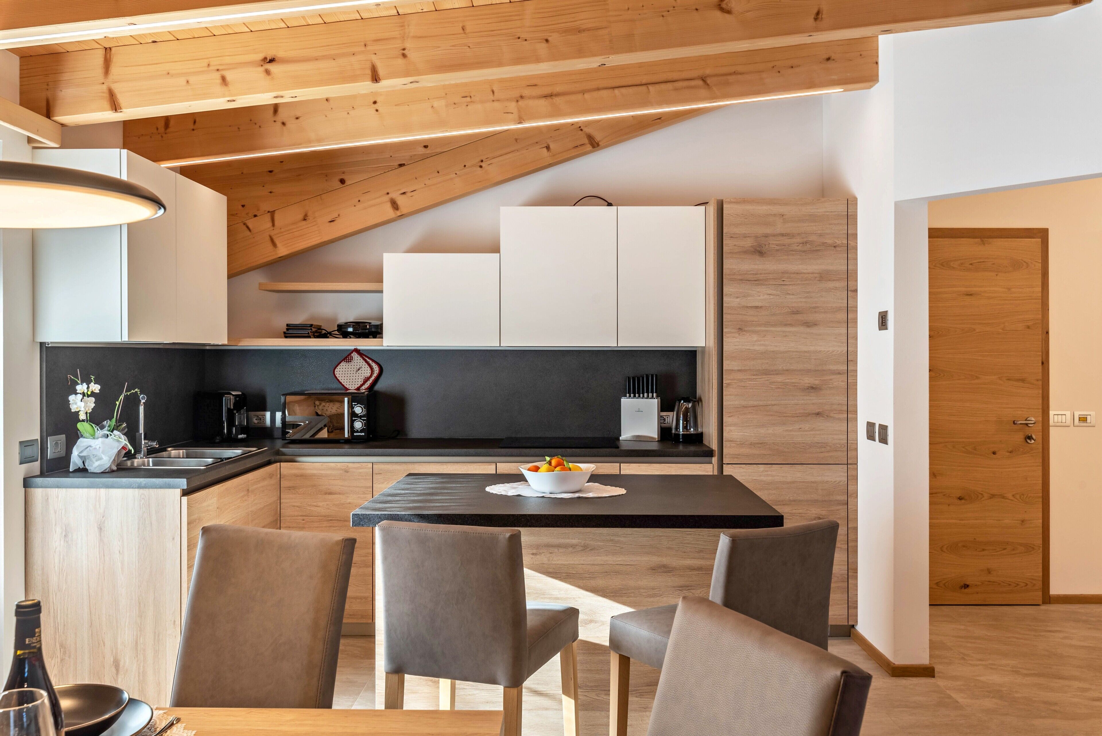 Una cucina moderna con zona pranzo, travi in legno a soffitto e piano di lavoro nero.