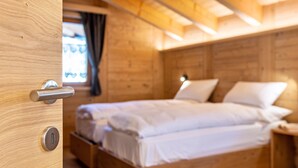 A wooden room with a bed, a window with curtains, and a door with a handle.