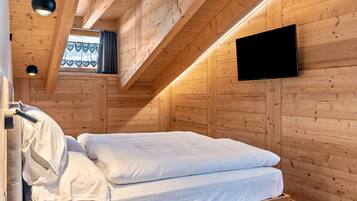 A wooden cabin room with a bed, a television mounted on the wall, and a window with curtains.