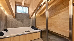 A modern bathroom with a freestanding bathtub, wooden paneling, a glass shower enclosure, and a stone-tiled floor.