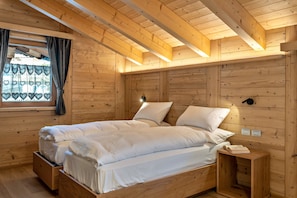 Une chambre dans une cabane en bois, avec un lit, une table de chevet et une fenêtre avec des rideaux.