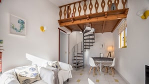 Un intérieur moderne avec un escalier en colimaçon, un coin repas et un canapé agrémenté de coussins à motifs.