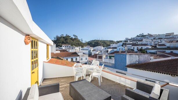 Une terrasse sur le toit, meublée de mobilier en osier, avec une porte jaune et une vue sur une ville aux bâtiments blancs.