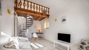 Une pièce comprenant un lit, un téléviseur, une table à manger avec des chaises, un escalier et un balcon.