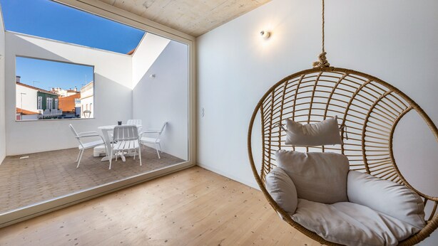 Un intérieur moderne avec un fauteuil suspendu, un coin repas et une vue dégagée sur l’extérieur grâce à une grande fenêtre.