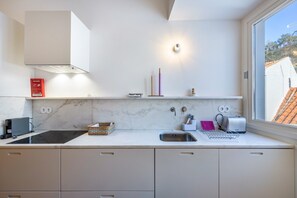 A modern kitchen with a built-in stove, a sink, and a window with a view of buildings.