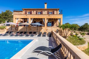 Uma área de piscina com espreguiçadeiras, uma piscina e um edifício de pedra com varandas.