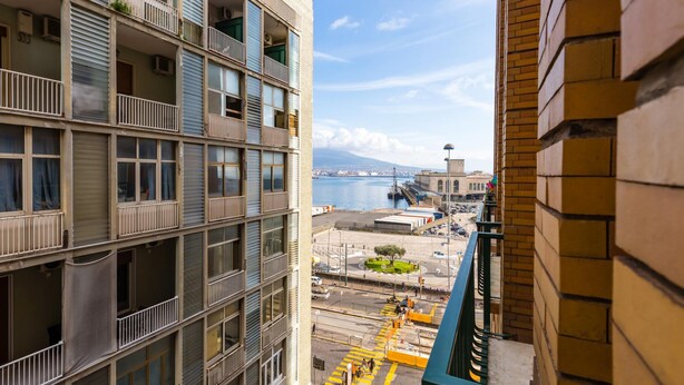 A multi-story building with balconies, a view of a harbor, and a distant mountain range. - Piazza Municipio Blue Apartment by Wonderful Italy (Naples)