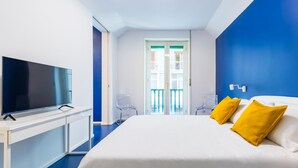A modern hotel room with a large bed, a flat-screen TV on a white console, a balcony with glass doors, and a blue accent wall. - Piazza Municipio Blue Apartment by Wonderful Italy (Naples)