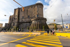 Um castelo histórico com uma grande torre central, rodeado por uma área pavimentada com marcações amarelas.