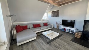 Een moderne woonkamer met een grijze modulaire bank, een witte salontafel, een flatscreen televisie en een open haard.