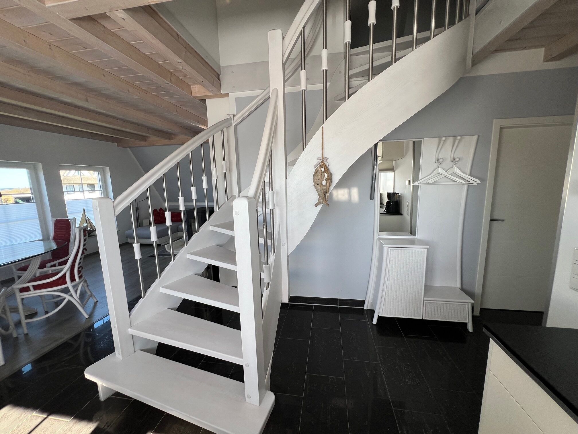 Un intérieur moderne avec un escalier blanc, un coin repas avec des chaises rouges et un espace cuisine.