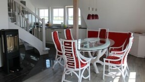 Een modern interieur met een ronde glazen tafel omringd door witte stoelen met rode kussens, een trap en een keukenhoek.