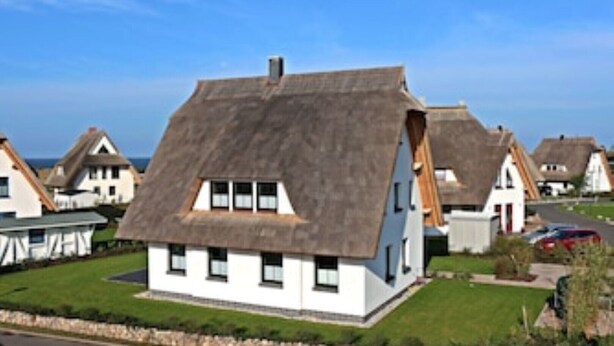 Een rij traditionele huizen met rieten daken en witte muren, met een stenen muur op de voorgrond.