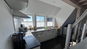 Een moderne keuken met witte kastjes, een zwart aanrecht en een raam met uitzicht op een witte schutting.