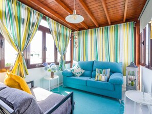 A room with a blue sofa, a small round table, a bed, and a window with striped curtains.